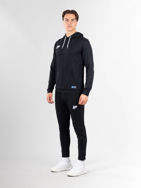 A man is standing up in a black hoody and black tracksuit bottoms