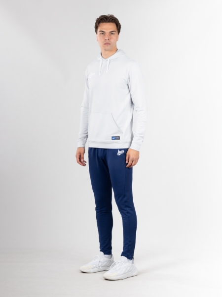 A man is stood looking at the camera in a light grey hoodie and navy tracksuit joggers