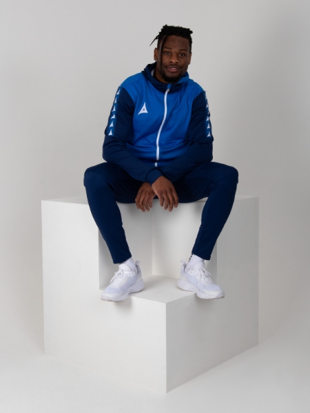 A man is stat down on a cube wearing a two-tone blue hoody