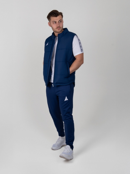 A man is standing up and looking into the distance wearing a navy gilet unzipped.