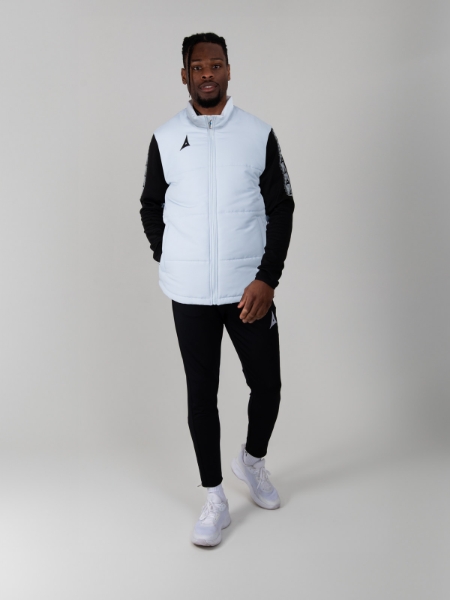 A man walking, wearing a light grey padded gilet and is matched with black tracksuit bottoms