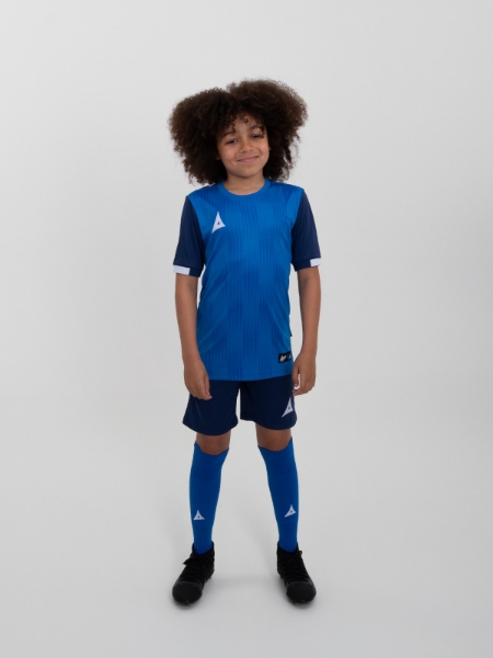 A young child is wearing a royal blue football kit, navy shorts and royal blue socks.