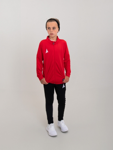 A boy is wearing a red tracksuit jacket and has combined this with black jogging bottoms