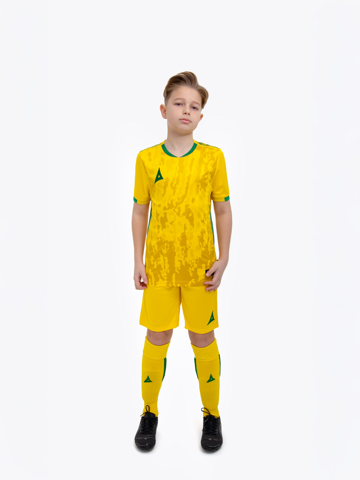 a kid standing up wearing a yellow and green football shirt, yellow shorts and yellow football socks.
