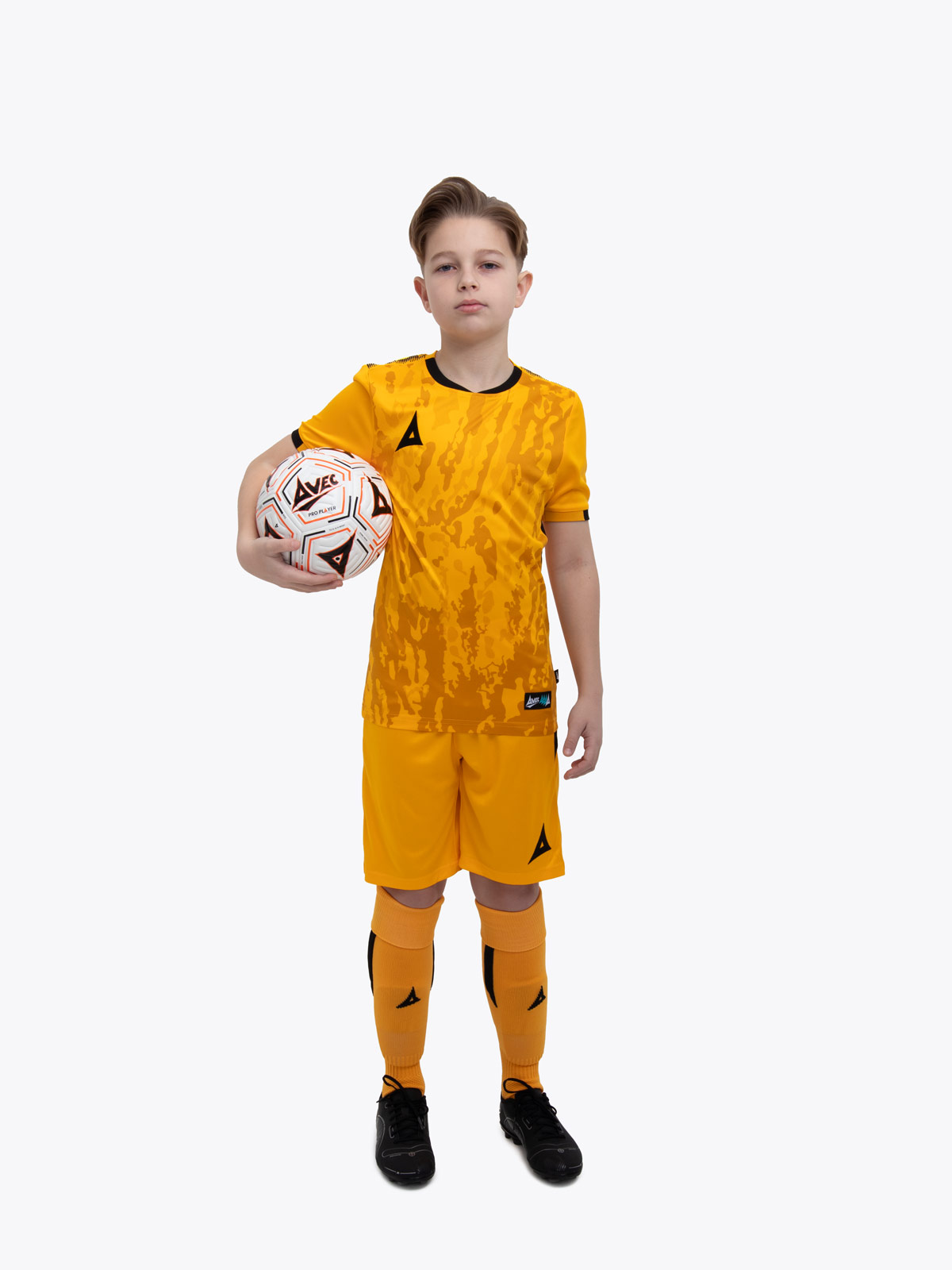 a kid standing up wearing an amber / black football shirt, matching amber shorts and amber football socks.