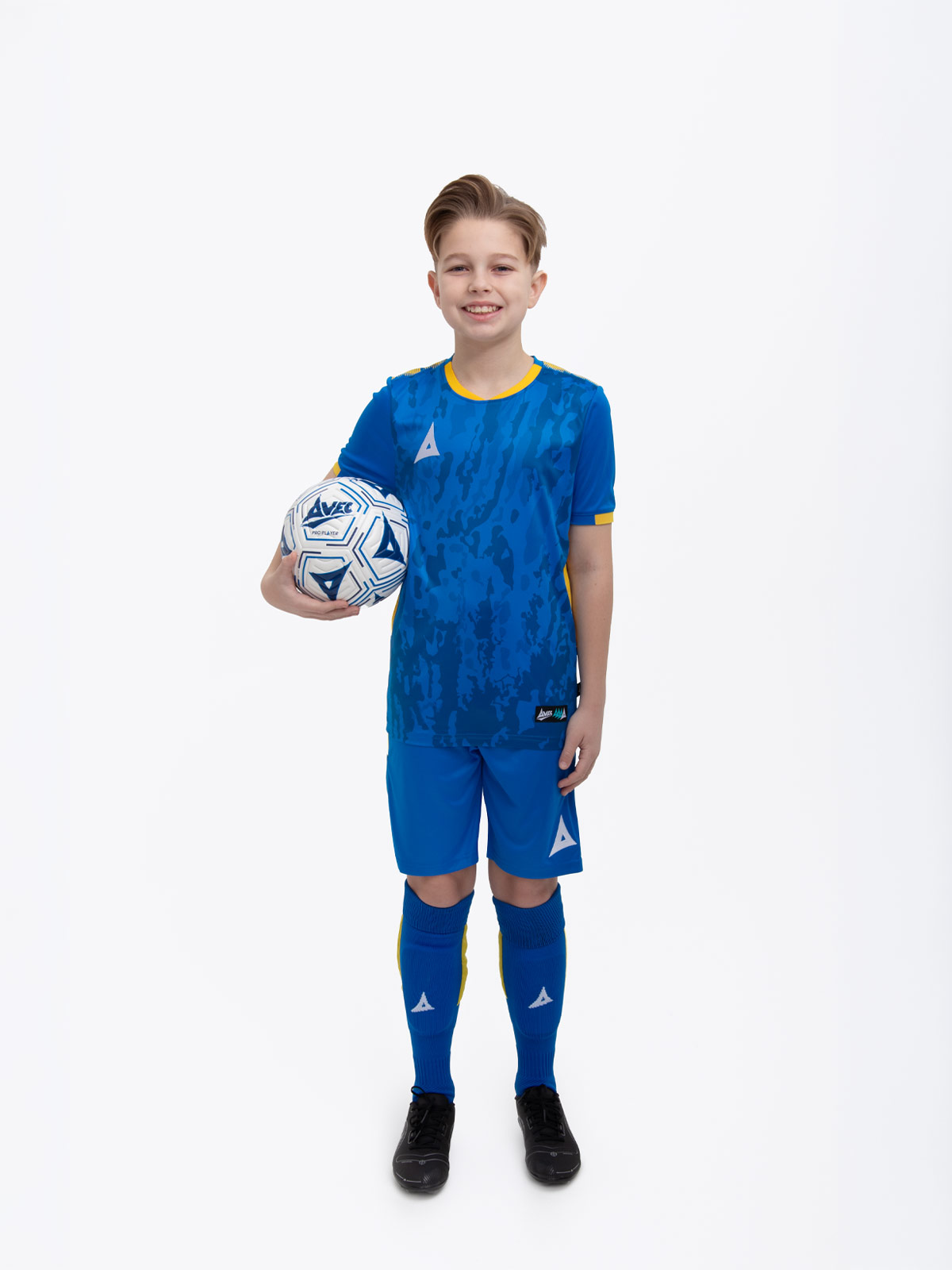 a kids football kit in royal blue and yellow with matching blue shorts and socks holding a football