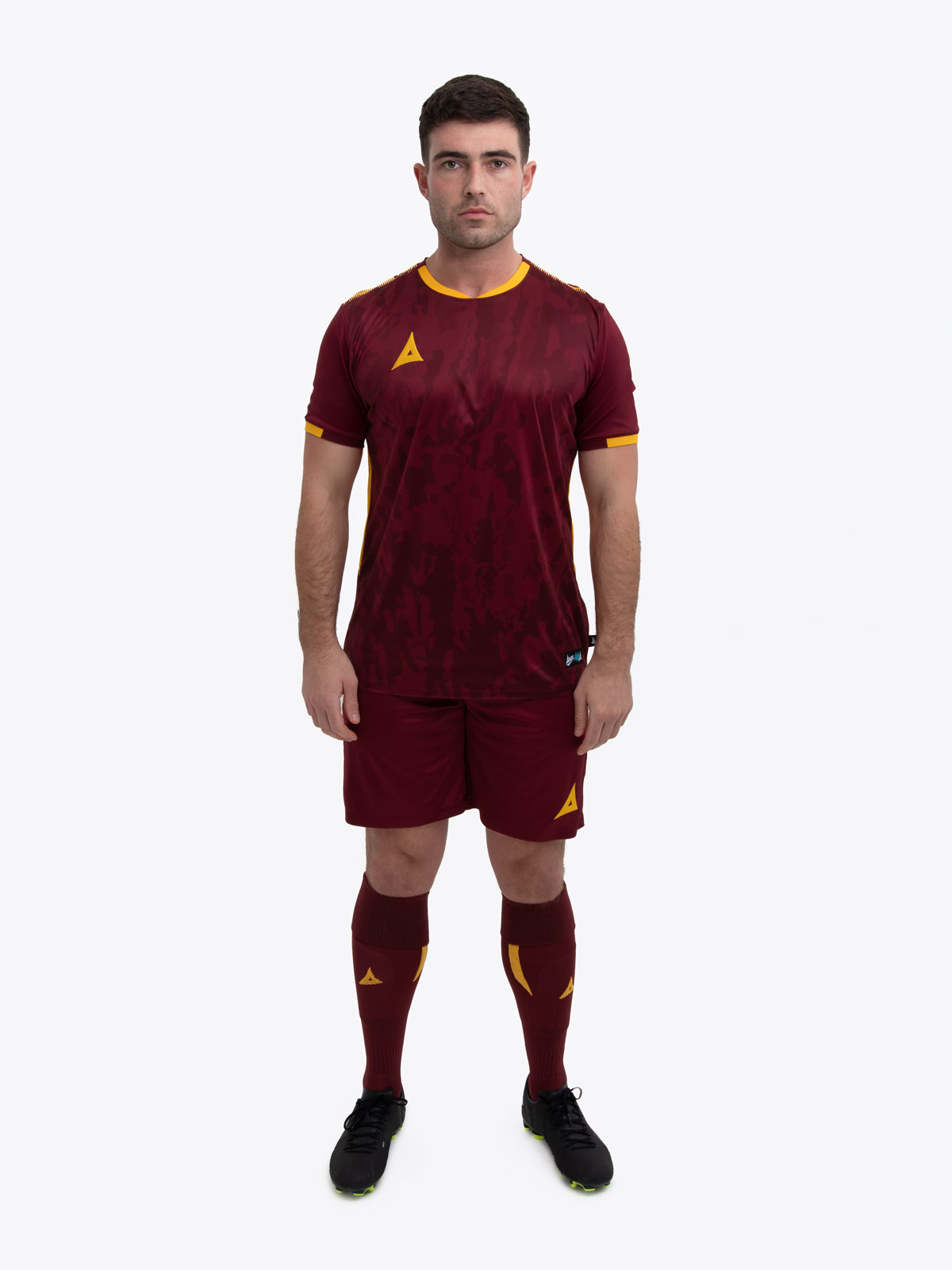 a model standing up wearing a claret / maroon football shirt, claret shorts and claret football socks.