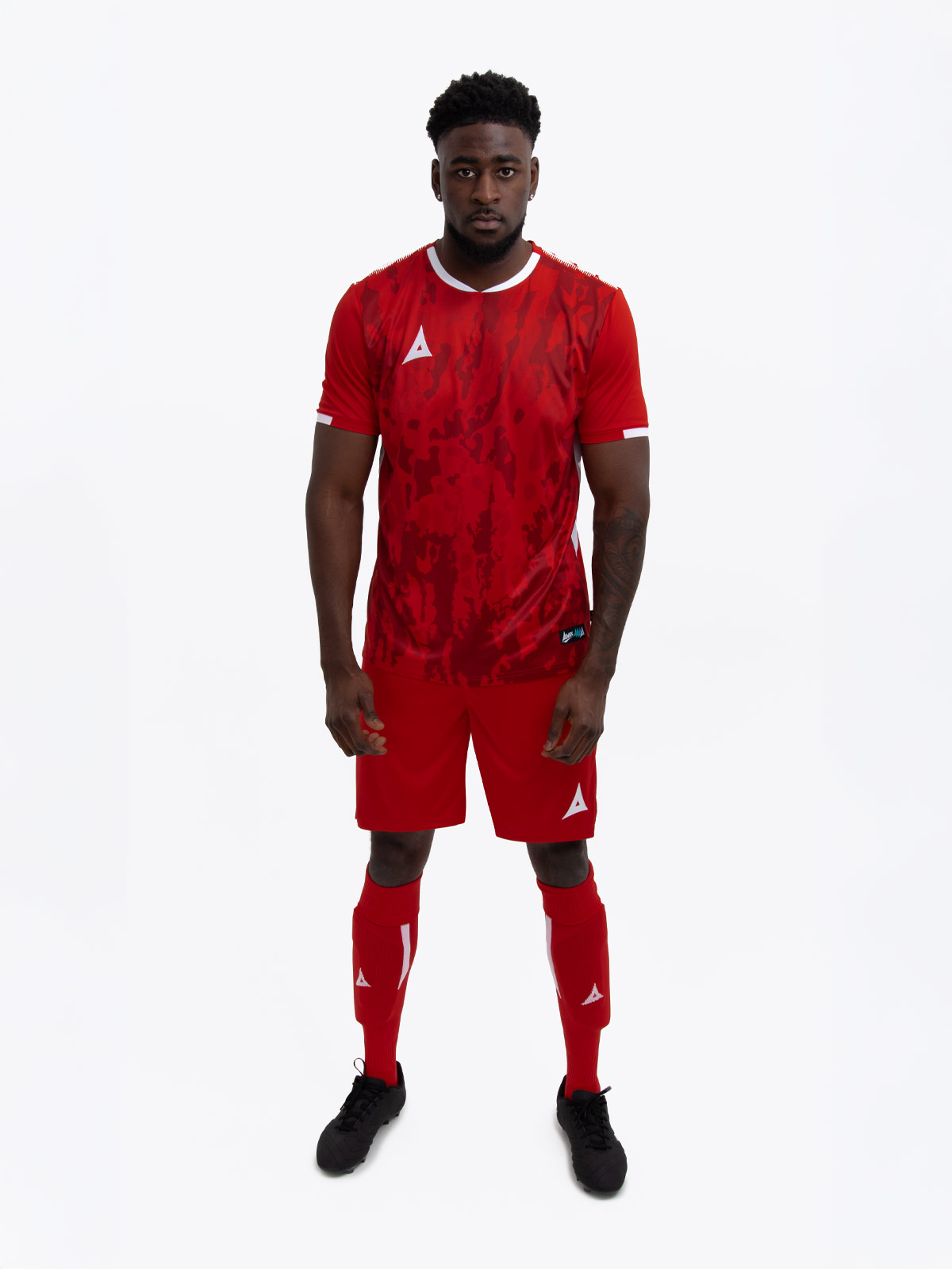 a model standing up wearing a red football shirt, matching red shorts and red football socks.