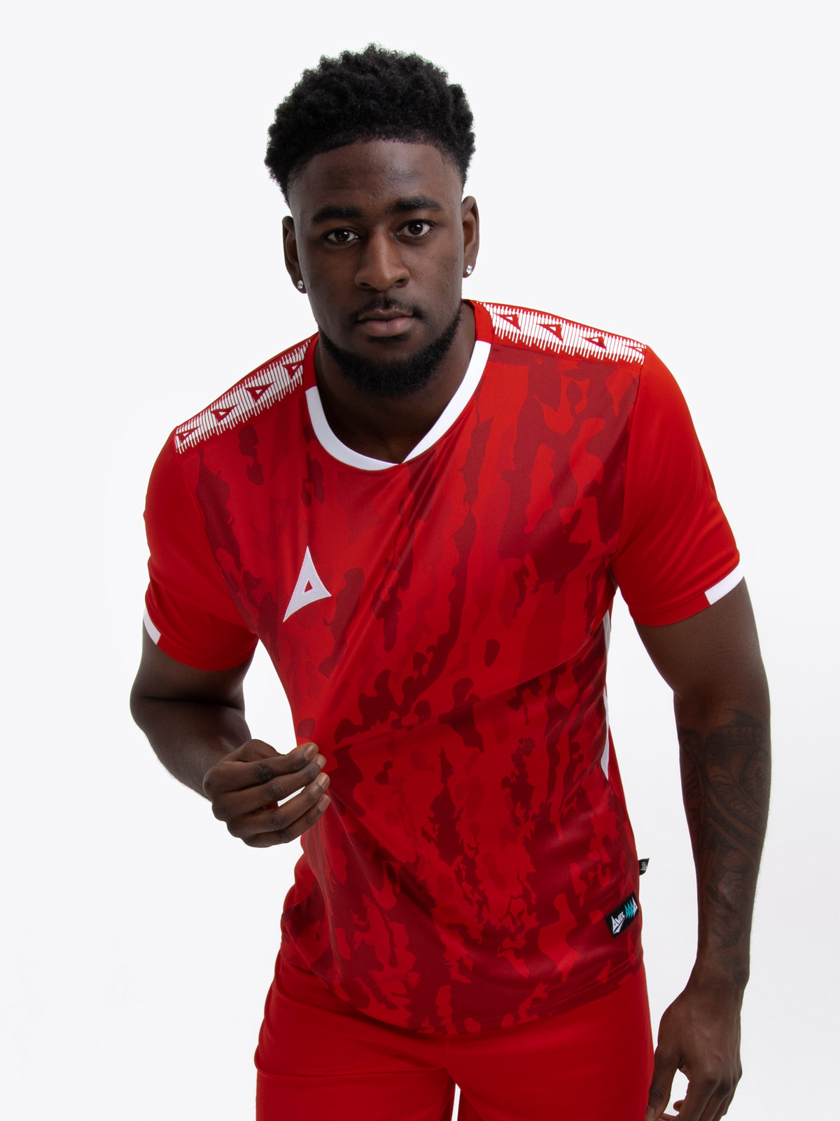 a man standing up wearing a red football shirt, matching red shorts and red football socks.