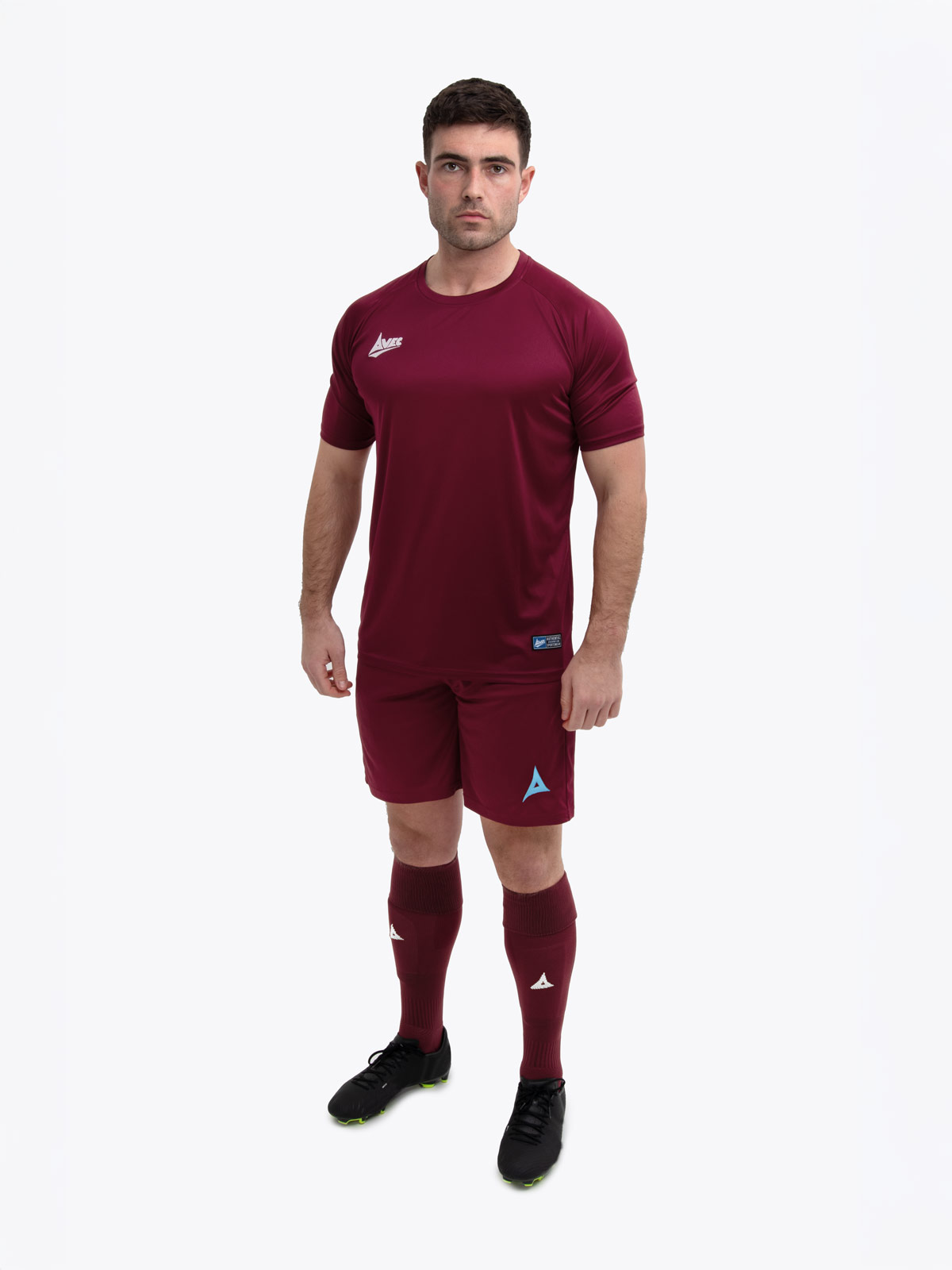 a model standing up wearing a claret / maroon football shirt, matching claret shorts and claret football socks.