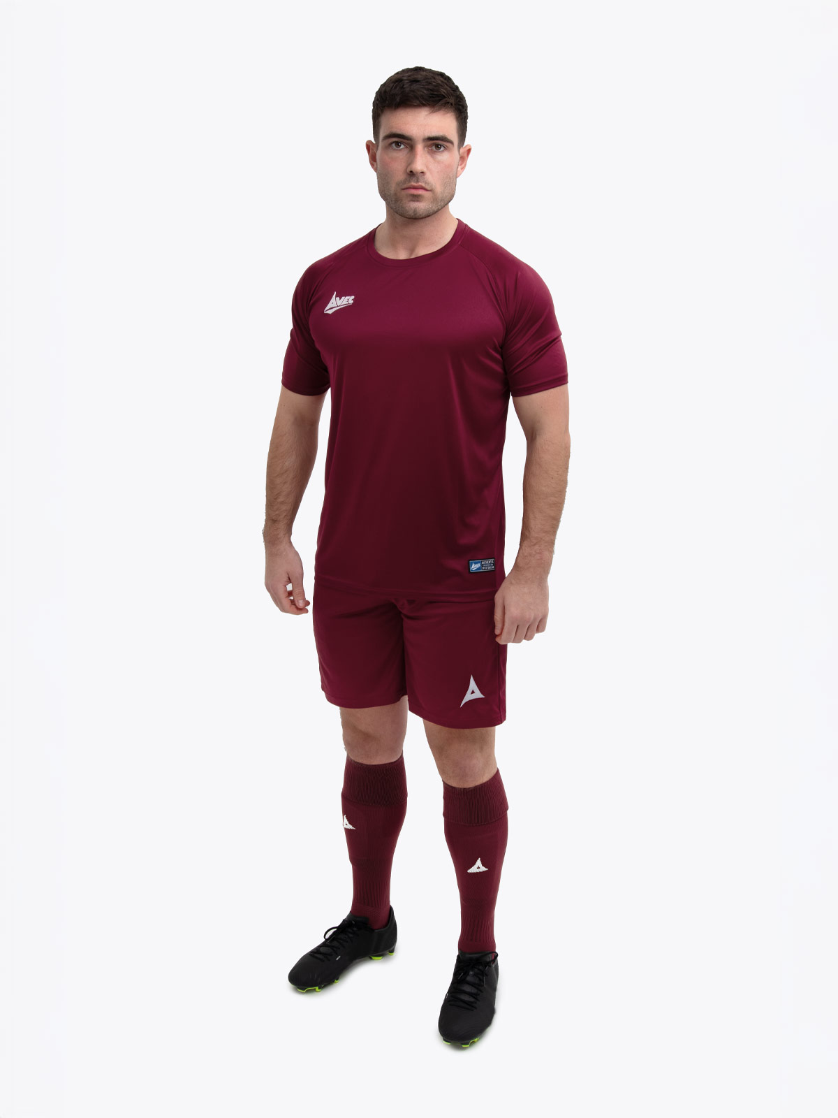 a model standing up wearing a claret / maroon football shirt, matching claret shorts and claret football socks.