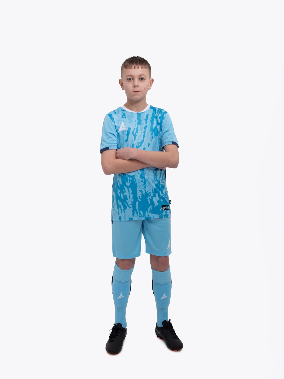 a kid standing up wearing a sky / navy football shirt, matching sky shorts and sky football socks.