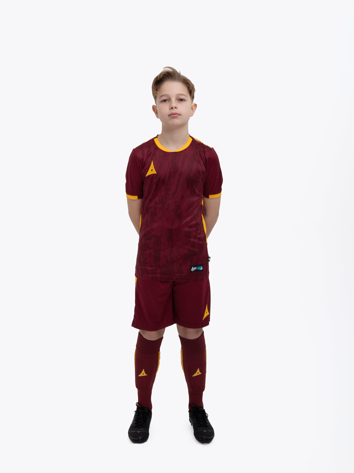 a child standing up wearing a claret and amber football shirt, shorts and football socks.