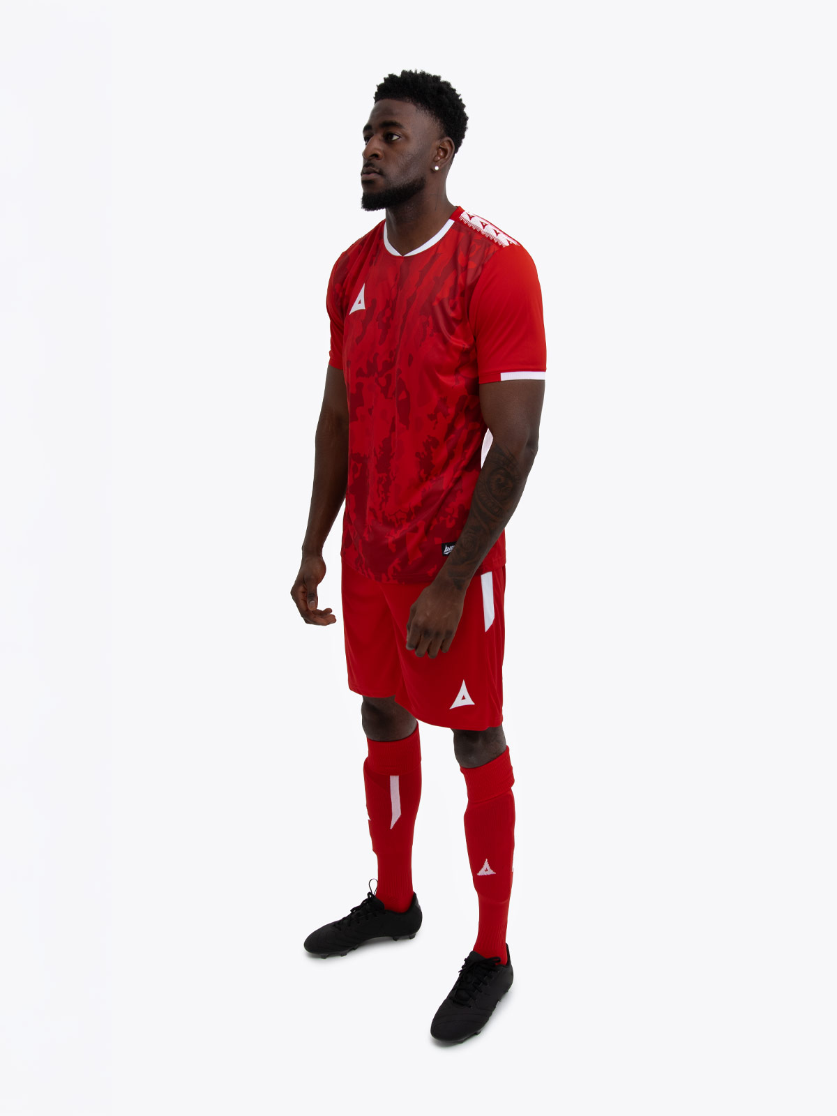 a model standing up wearing a red football shirt, matching red shorts and red football socks.