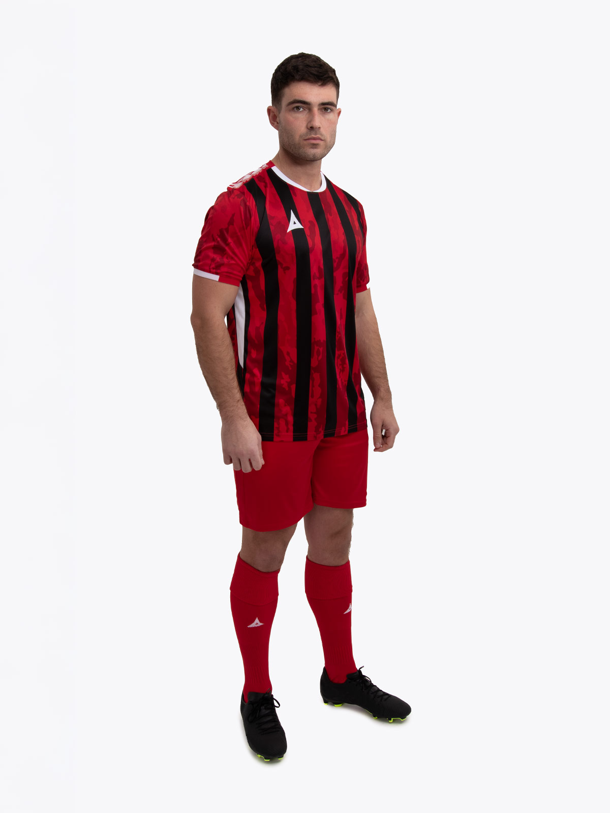 a model standing up wearing a red and black football shirt, red shorts and red football socks.