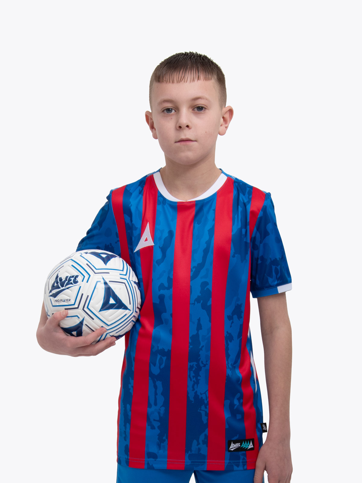 a kid standing up wearing a red and royal blue football shirt and holding a royal blue and white football