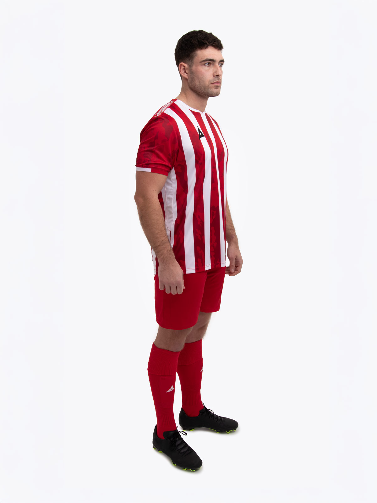a model standing up wearing a red and white football shirt, red shorts and red football socks.