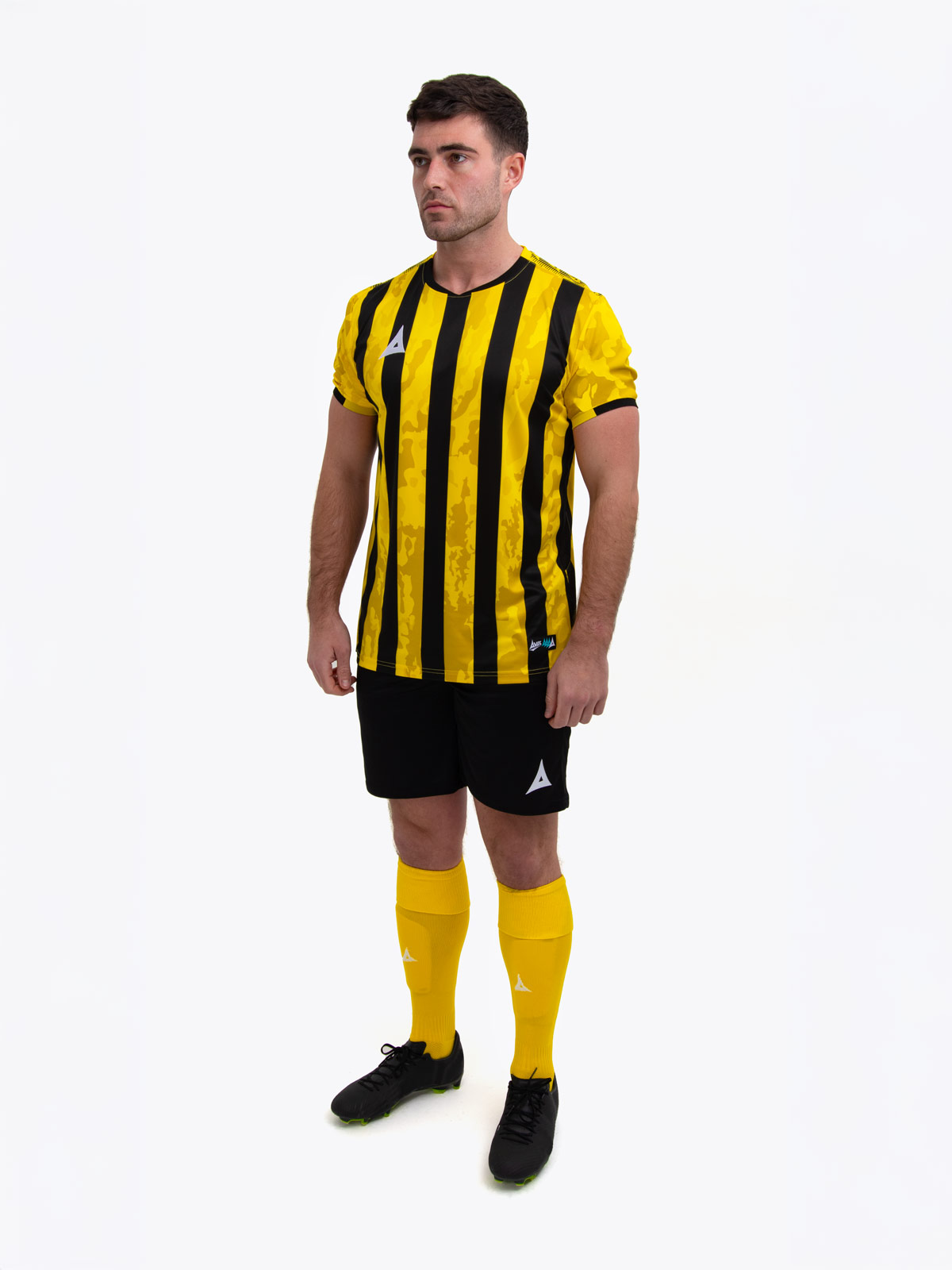 a model standing up wearing a yellow and black football shirt, yellow shorts and yellow football socks.