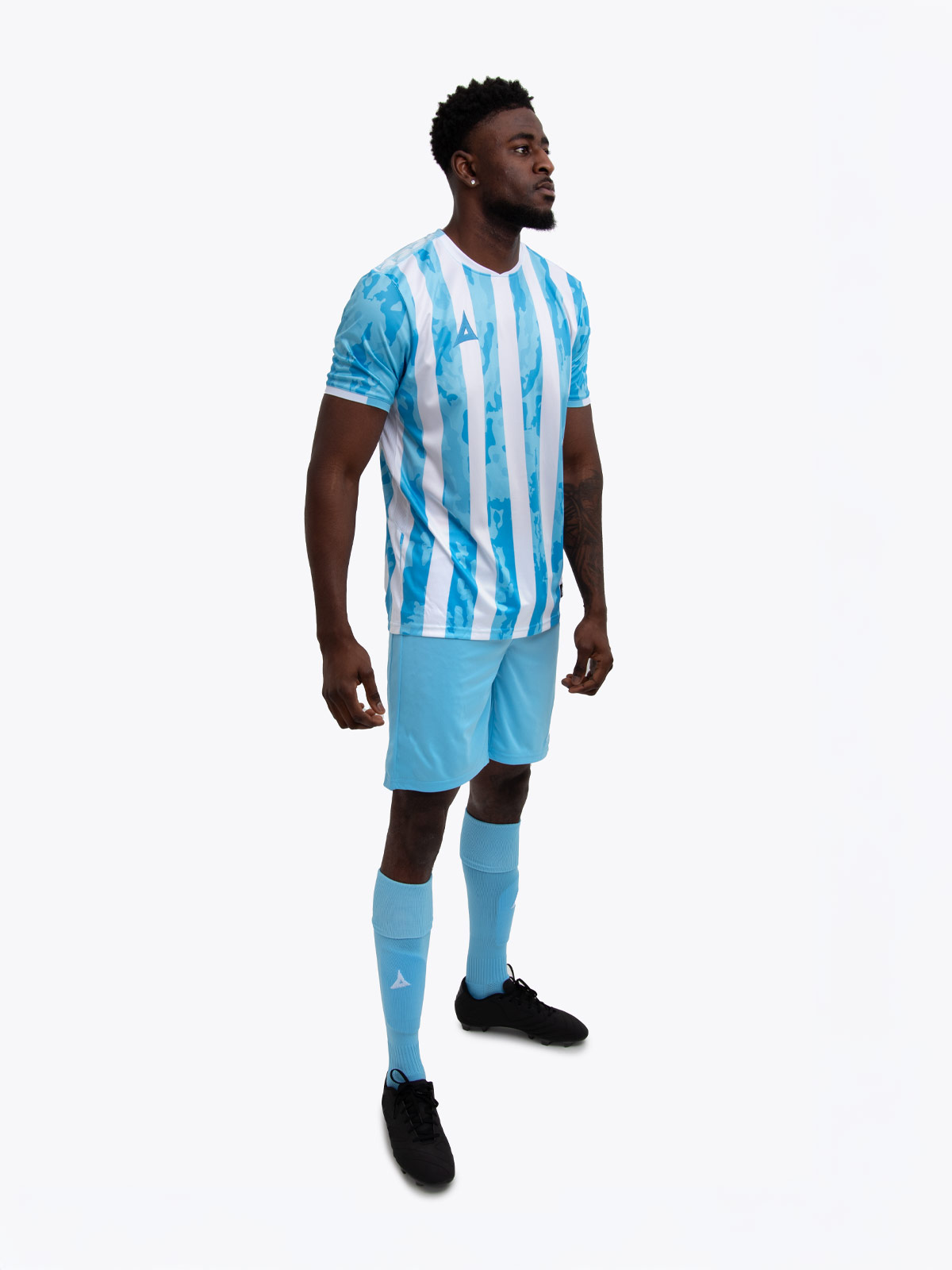 a model standing up wearing a hyper sky and white football shirt with white stripes, hyper sky shorts and hyper sky football socks.